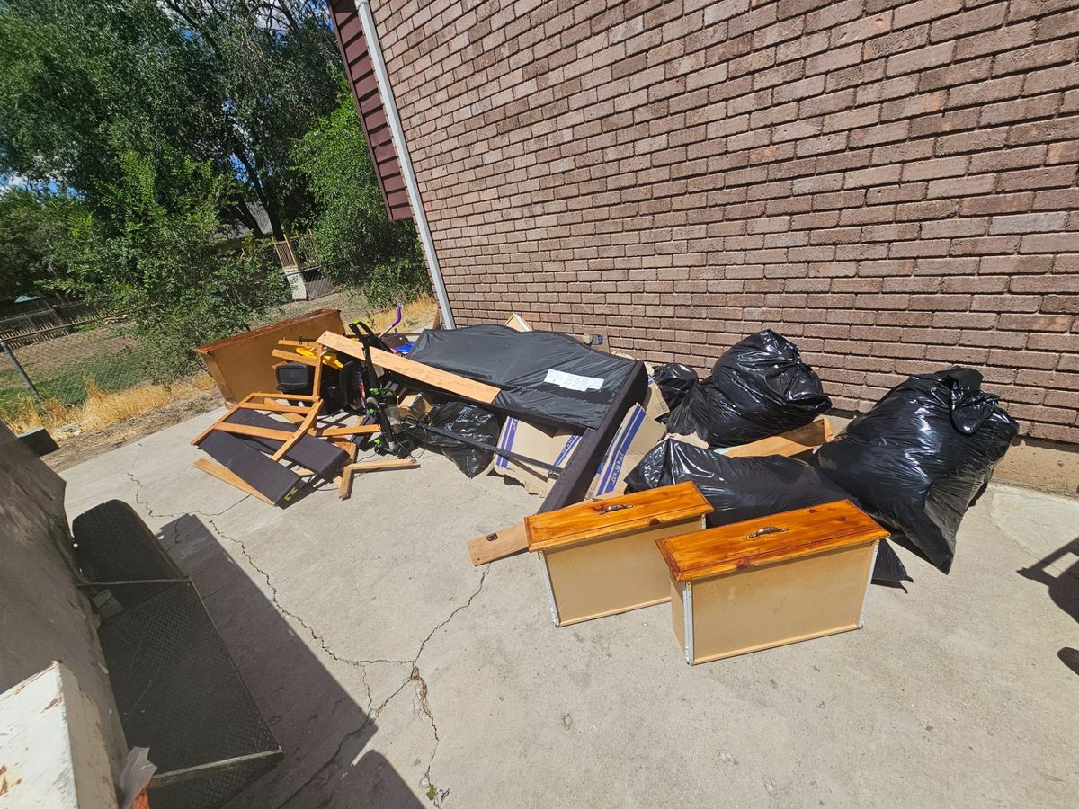 Unwanted furniture, drawers, and bagged items beside a brick wall