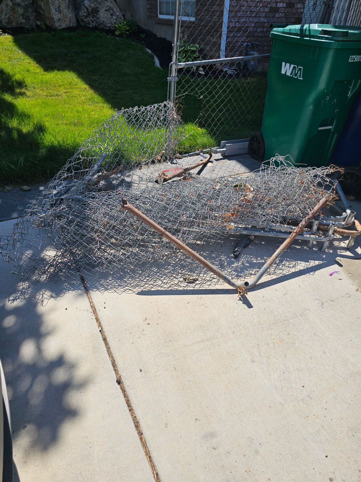 Chain-link fencing and metal posts gathered on a driveway for removal